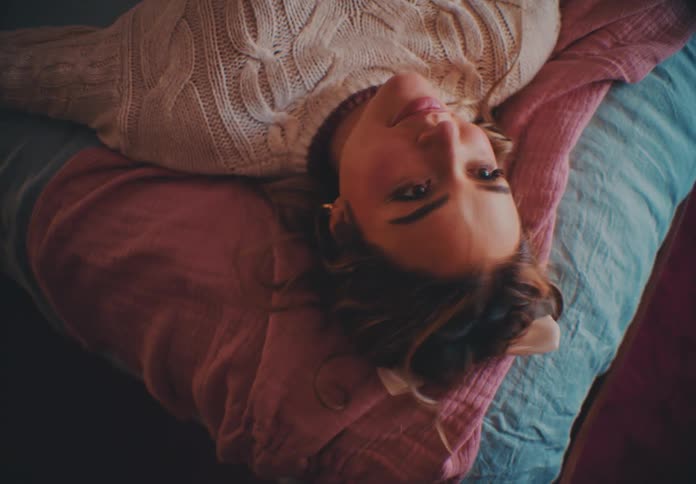 The face of a young woman who is smiling while lying on a bed