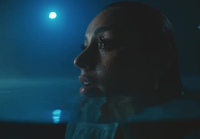 Woman wearing clothes while partially submerged in water at night trembles and stares