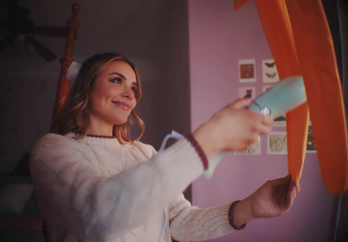 Woman steams a pair of orange tights hanging in a bedroom