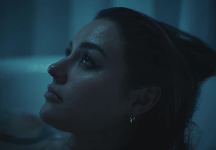 Woman wearing earrings soaks in the bathtub in a dimly lit bathroom