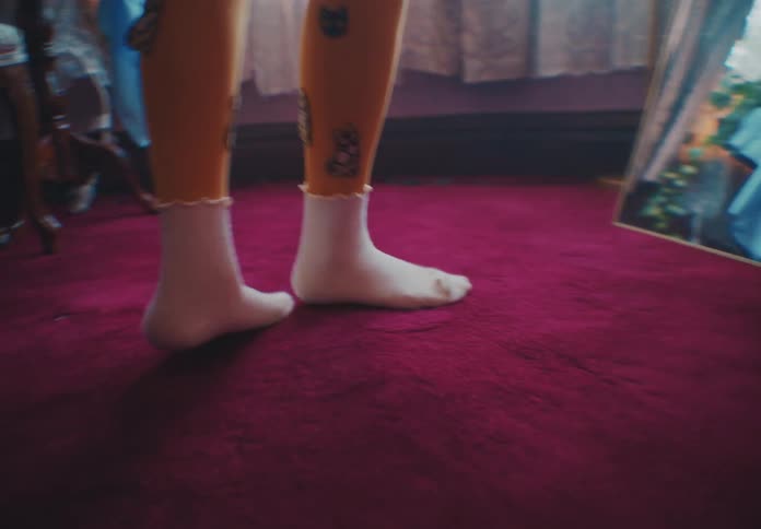 A young female in her room wearing a sweatshirt and yellow tights dances in front of a mirror