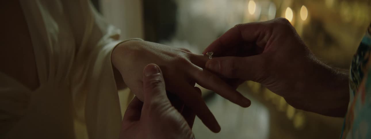 A closeup moment where one person is placing an engagement ring with a prominent gemstone onto anothers finger