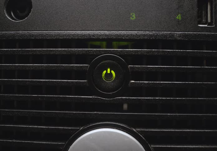 A green power button on a dark computer panel glows then fades off in a closeup shot