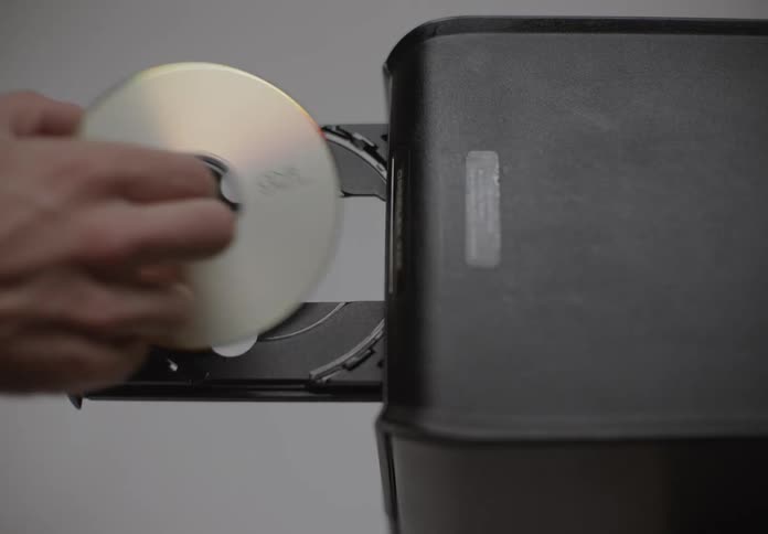 A hand is inserting a compact disc into the open tray of a black computer