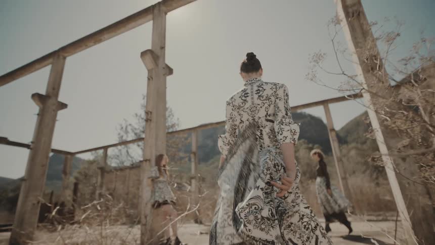 Three young women wearing fashionable dresses in an unfinished structure with mountains in the background