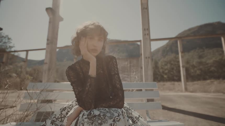 Woman in dress sitting on white bench outdoors with mountains in background