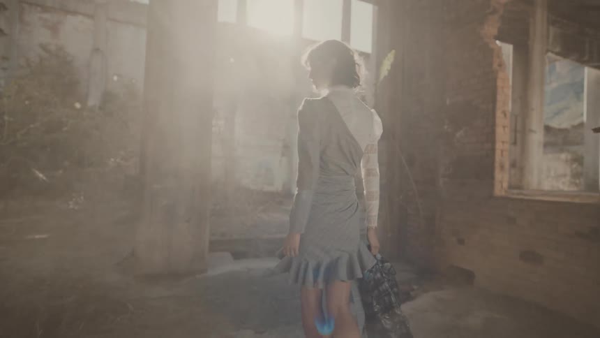 A woman in a lightcolored dress is walking in the bright sunlight filtering through the openings of a dilapidated building
