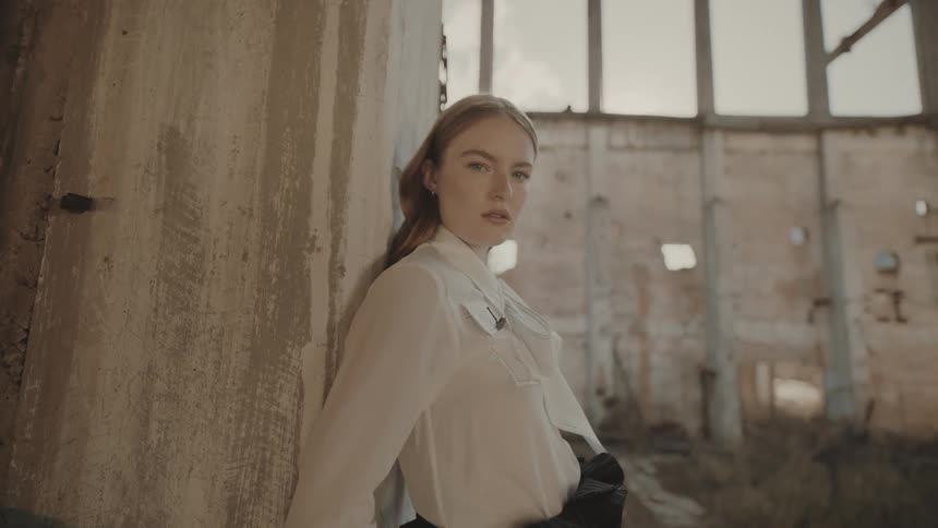 Woman leaning against a concrete wall looks out into an abandoned building illuminated by the evening light