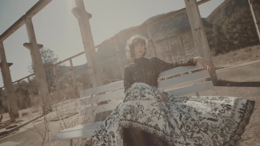 Woman in dress and skirt sitting on a bench outdoors with mountains in the background