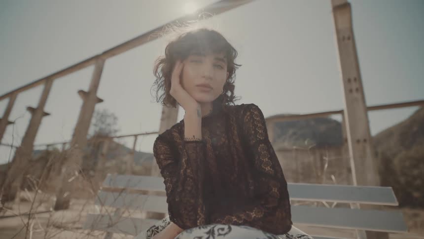 Woman sitting on a bench in the sunlight resting her hand on her face with a piercing gaze
