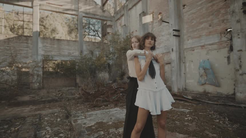 Two young women wearing fashionable clothes embrace each other in an unfinished building