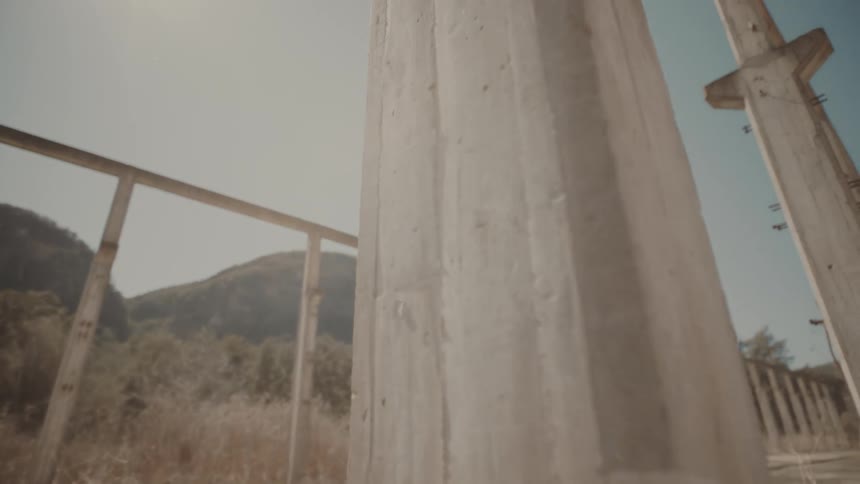 Unfinished concrete structure on a barren land is illuminated by sunlight with mountains in the background