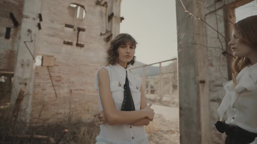 Two female models pose in an abandoned sunlit building with a moody fashionforward atmosphere