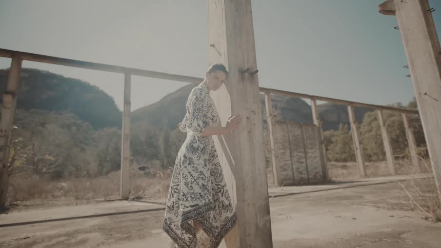 Woman leaning against an unfinished concrete structure with mountains in the background