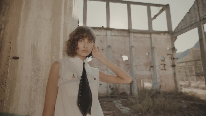 Woman in renata and black tie leaning against a wall of an unfinished structure