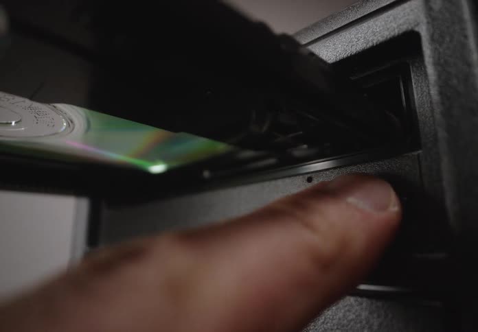 A hand opens a computers cd rom drive and inserts a disc then closes the drive