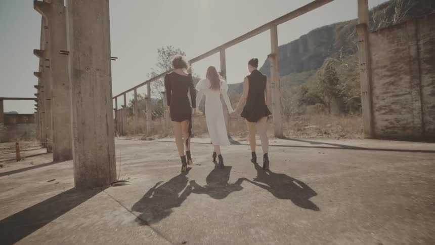 Three women walk confidently through a deserted concrete structure suggesting a fashion shoot or performance