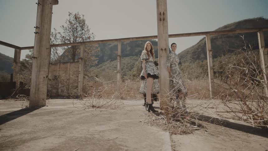 Three models stand and pose beside a pillar in a roofless ruined building on a sunny day all wearing identical clothing