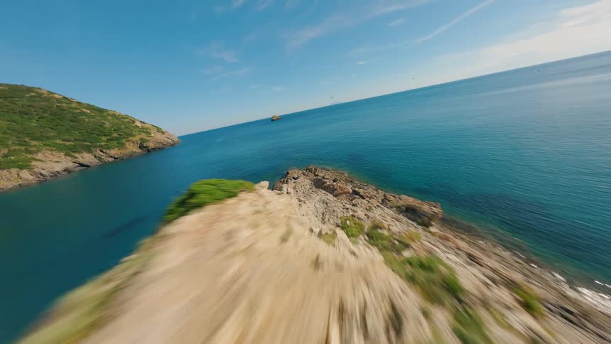 Flying through a small gap towards a blue ocean coastline