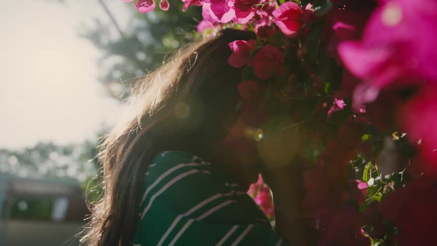 A girl stands closely beside vibrant pink flowers partially hidden possibly in a moment of emotion or reflection