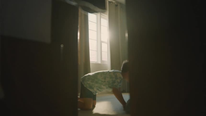 Boy looks under the furniture and in the closet while playing hide and seek during the daytime