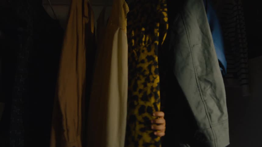 Girl walks into a room and hides behind the clothes hanging on a closet rod