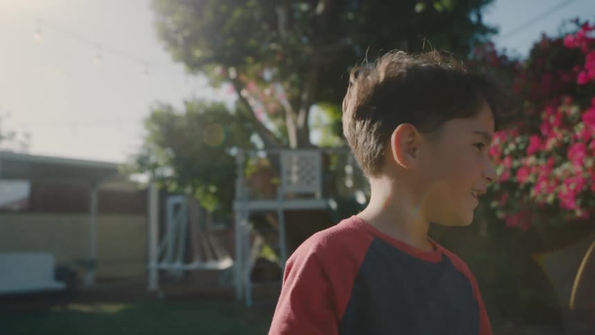 A young boy covers his eyes while counting during a game of hide and seek in a sunny backyard