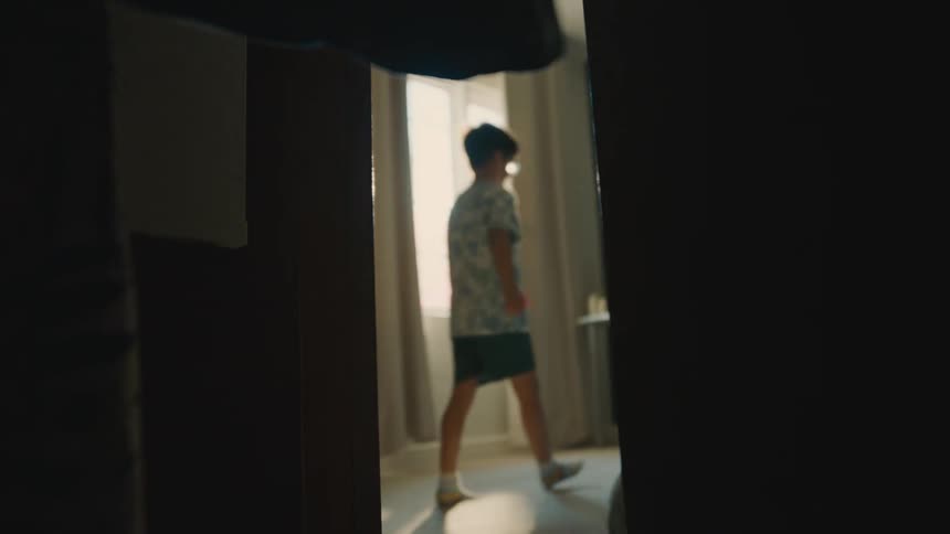 Boy walking through a room in a house seen through clothes in a closet