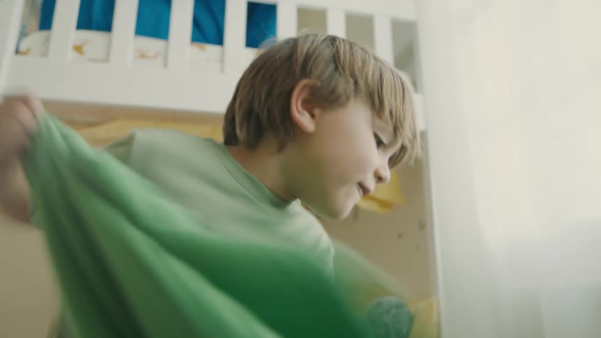 A young boy excitedly laughs as he pulls away a green blanket discovering someone or something hidden
