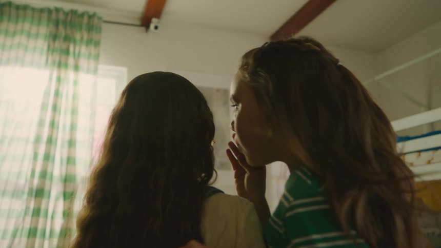 Two girls whispering in each others ears in a room