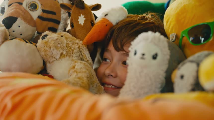 A smiling child is hiding among a pile of stuffed animals