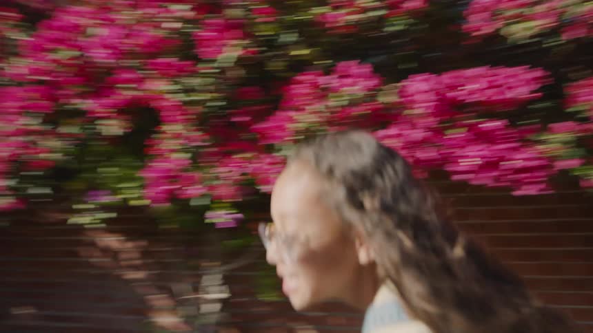 Two girls is running joyfully past vibrant pink flowers in a sunny backyard setting