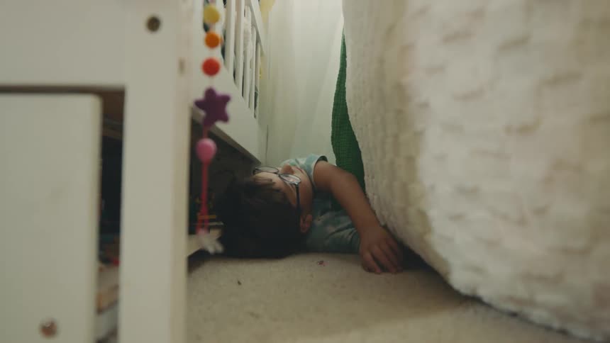 A boy lying on the bedroom floor near a crib