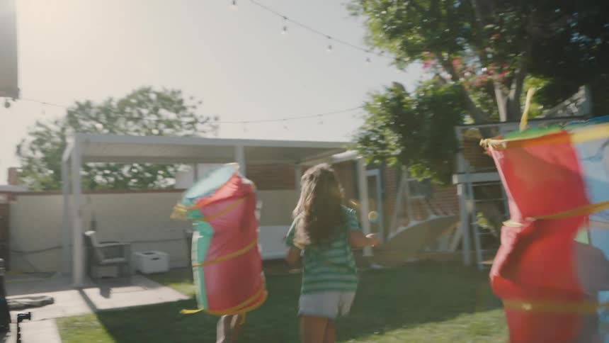 Children are joyfully running and playing in a sunny garden beside a blooming pink flower wall
