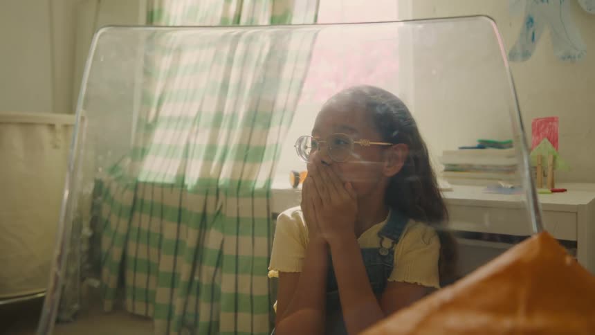 A young girl looks surprised and delighted as she peers through a clear barrier indoors