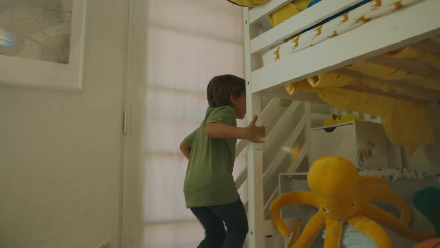 Happy boy climbing up the ladder of a crib in his room
