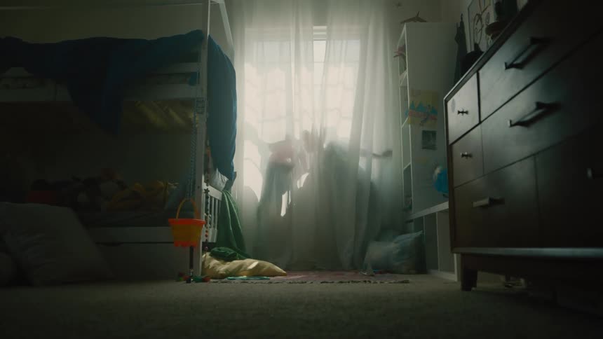 Two kids are playing behind a curtain in a softly lit bedroom