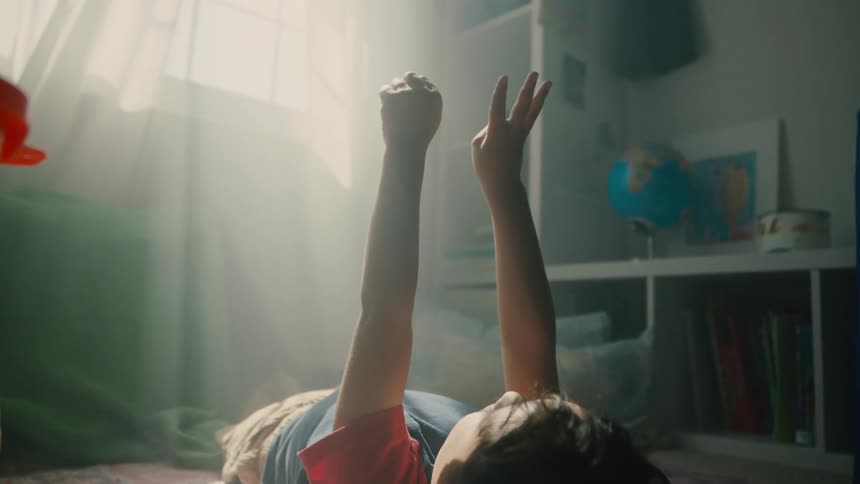 A child lying on a rug in a bedroom with hands raised making numbers with their fingers
