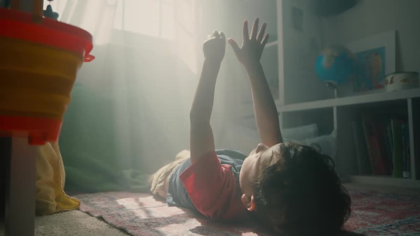 Little boy lying on a rug with his hands up and a reflection of sunlight coming through the window