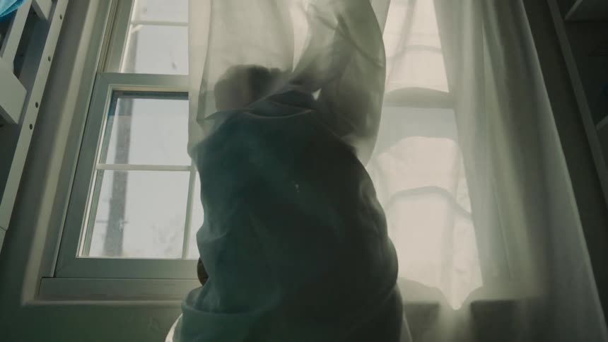 Two kids playfully hug while wrapped in curtains standing by a sunlit window