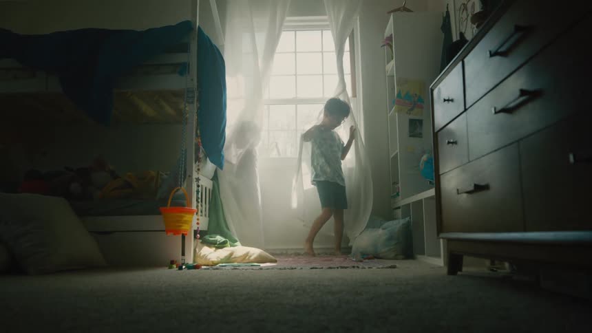 Two young male siblings play in their shared bedroom by twisting themselves into and out of the curtains