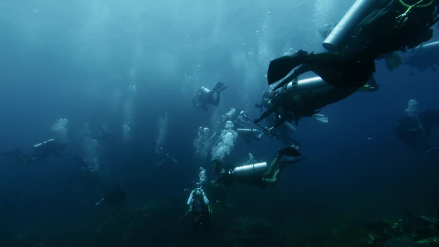 A group of scuba divers explores the depths of the ocean with visible bubbles rising towards the surface