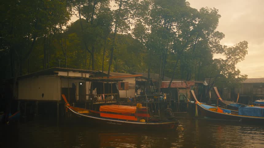 Stilted shacks and docked boats line a murky riverbank under an overcast sky