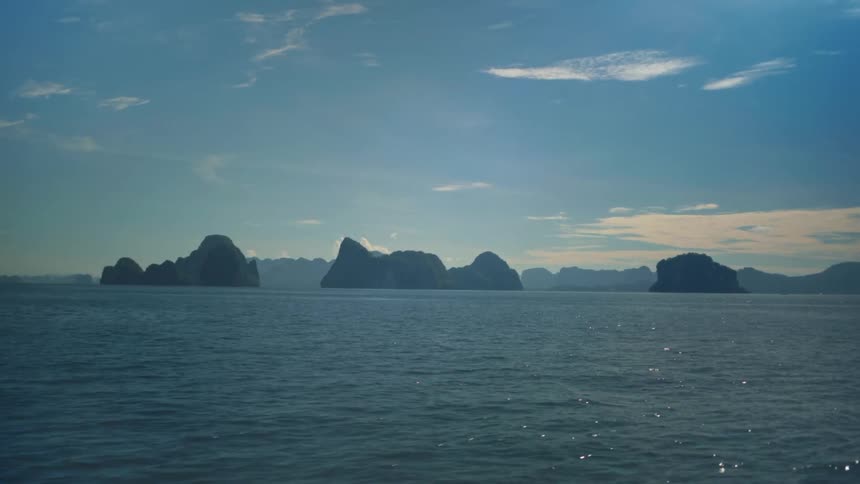 A serene seascape with several rocky islands silhouetted against a clear blue sky