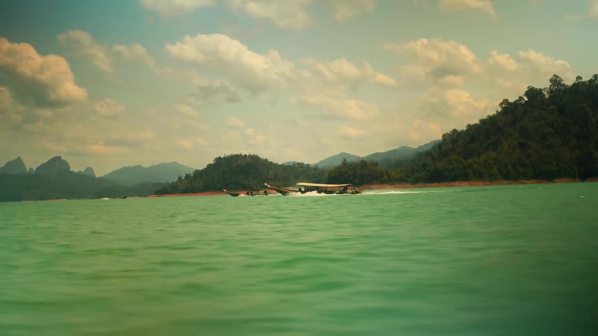 Motorized wooden boats traveling through green waters with mountains in the background