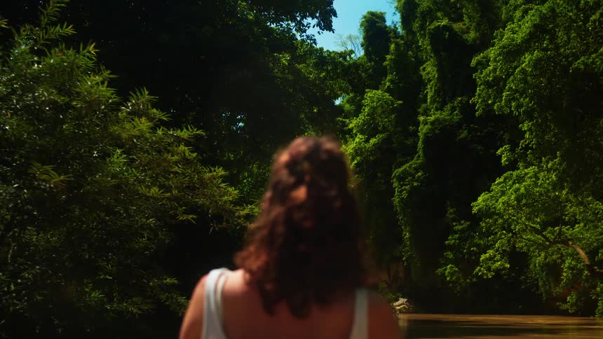 Woman riding in a boat looks at the dense forest crowding the riverbanks