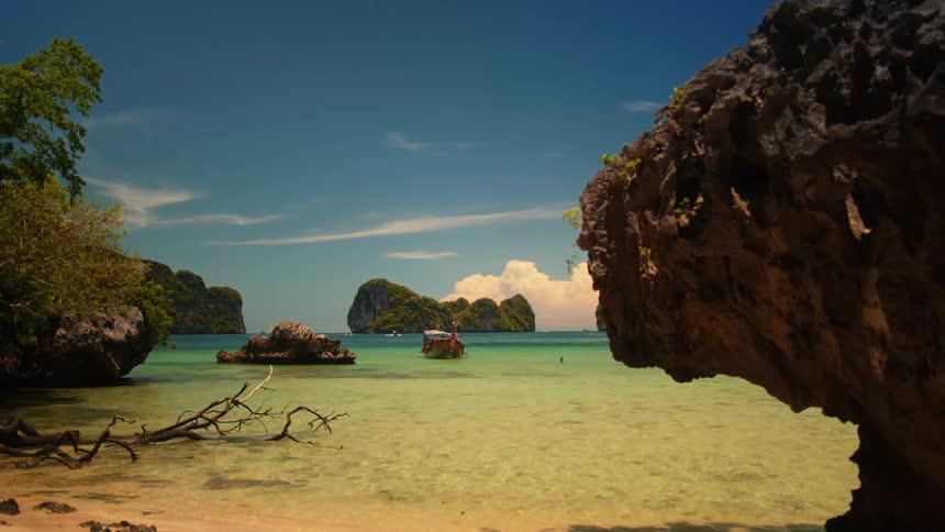 A serene tropical beach scene with limestone formations a boat on clear water and lush greenery under a bright blue sky
