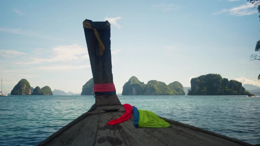 A wooden canoe with cloth tied to the bow sailing on the sea with other canoes and boats nearby
