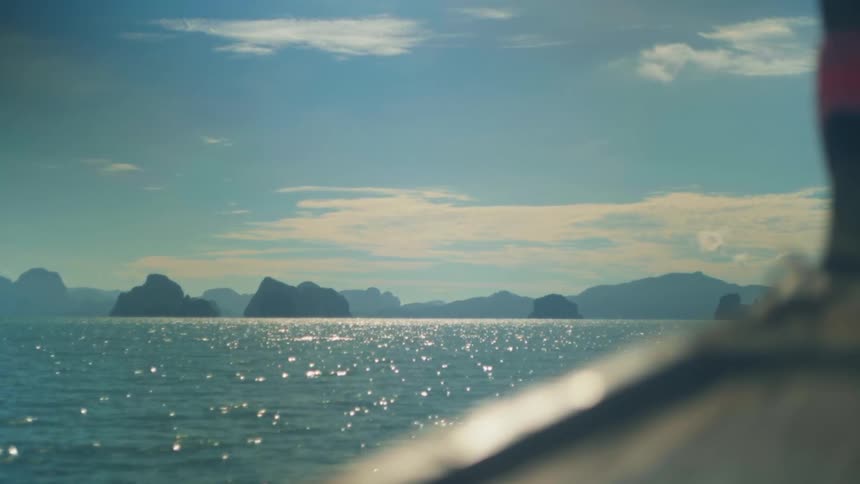 Watercraft heads across the sparkling water towards a mountainous coast on a cloudy day
