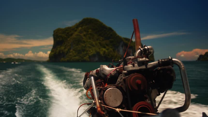 Motor powers a watercraft across the water leaving a wake that passes a forested island